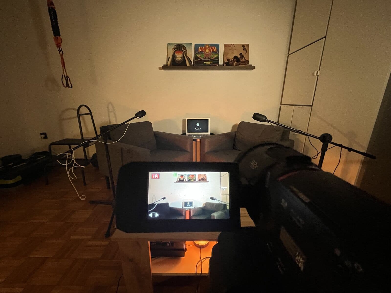A Metis stúdió a kamera mögül, meleg esti fényben: a kamera kijelzőjén a két fotel, a mikrofonok és a laptop a Metis logóval.