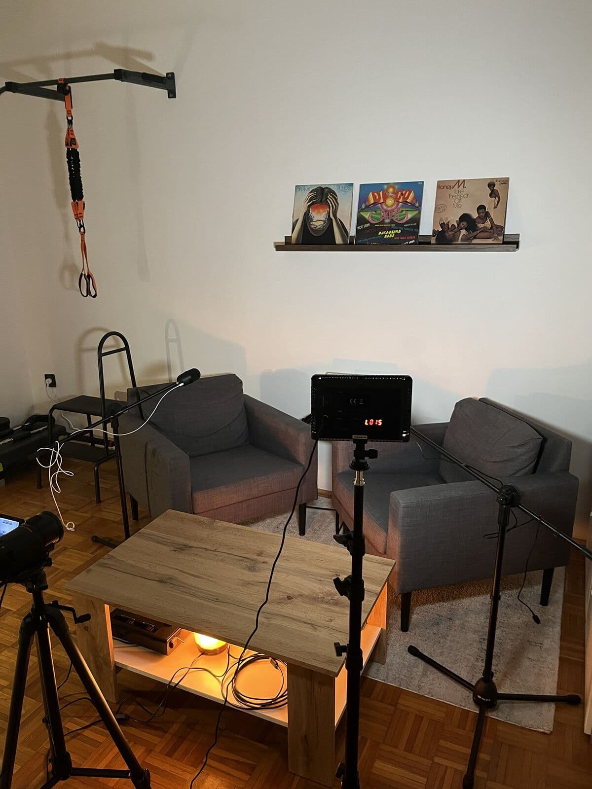 A stúdió oldalról: a fotelek, a dohányzóasztal alatt sólámpa, előtérben a LED-lámpa és a kamera állványa.
